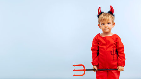 Happy cheerful boy in devil costume with trident on blue backgroundの写真素材