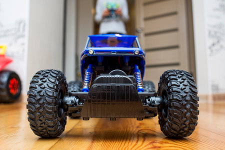 The boy is controling the blue toy car with a remote control.