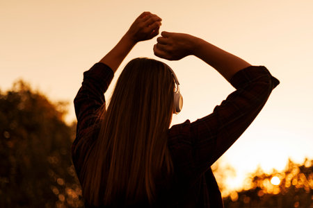 Silhouette of young woman in headphones enjoying music and dancing at sunsetの写真素材