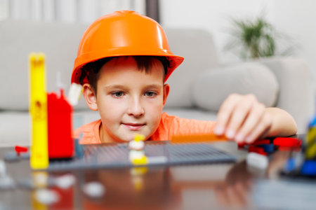 Child boy in helmet playing and building with colorful plastic bricks at table