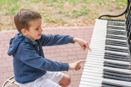 A little boy plays the street piano in the summer. Child playing pianoの写真素材