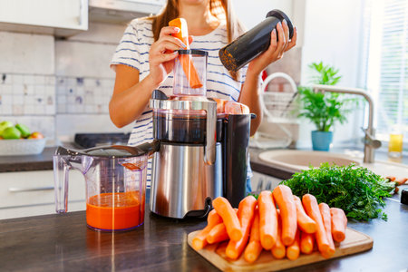 Woman preparing nutrient-rich carrot juice using juicer in the kitchen at homeの写真素材