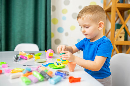 Little boy enthusiastically plays with plasticine, play dough on white tableの写真素材