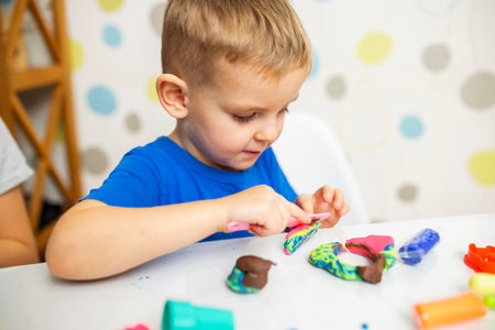 Little boy enthusiastically plays with plasticine, play dough on white tableの写真素材