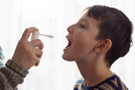 The child receives medication through a mouth spray for a sore throatの写真素材