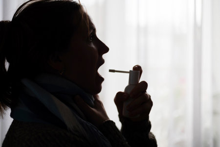 A woman with a sore throat sprays a medicinal aerosol spray down her throatの写真素材