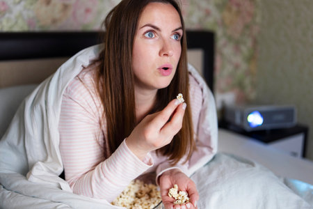 Woman Eating Popcorn Watching Movie at Homeの写真素材