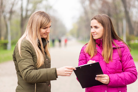Two women engaged in a conversation with a clipboard on a park pathの写真素材