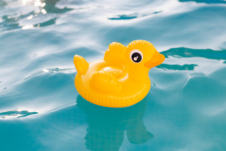Yellow inflatable duck floating on blue water in a pool on a hot summer dayの写真素材