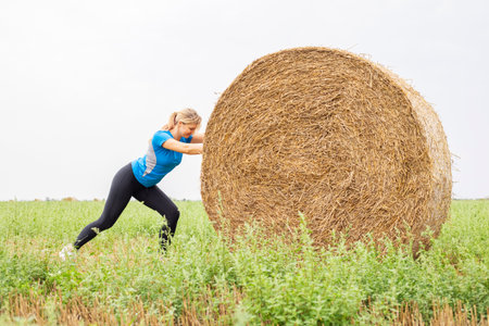Woman Exercising with Hay Bale in Fieldの写真素材