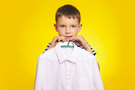 Boy Holding White Shirt on Hanger Against Yellowの写真素材