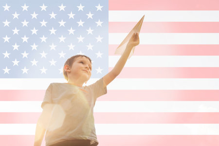 Little boy launches a paper plane into the air on the flag of america background. Child launches a paper plane with prideの写真素材