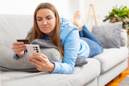 Woman in blue hoodie using credit card and smartphoneの写真素材