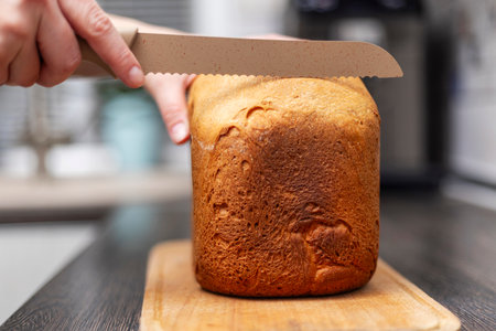 Hand slicing freshly baked bread with a bread knifeの写真素材