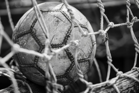 Close-up of an aged soccer ball in goal net. Vintage sports memorabilia concept for design and print.の素材