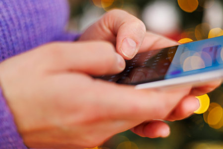 Woman typing on smartphone with Christmas lights