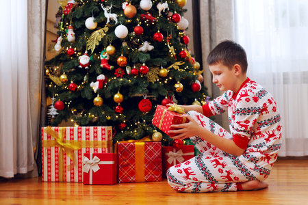 Boy opening gifts under Christmas tree in pajamasの写真素材