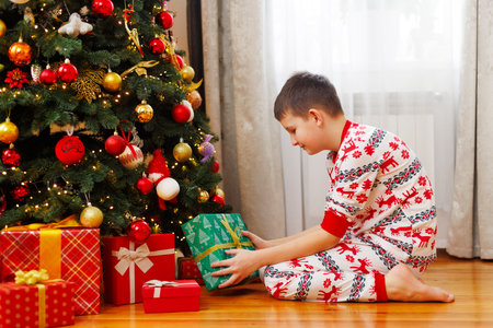 Boy in pajamas opening Christmas presents by treeの写真素材