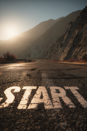 A mountain valley road at dawn features a prominent "START" marking illuminated by the rising sun, creating a motivational and cinematic atmosphere.の素材