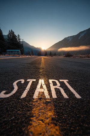 A scenic mountain valley road at dawn features a "START" marking illuminated by sunlight. The cinematic view captures the essence of new beginnings and motivation.の素材