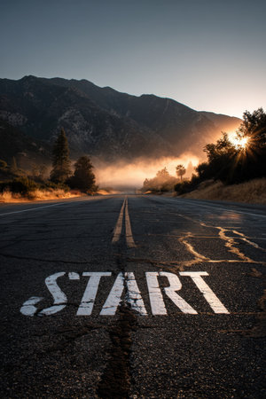 A cinematic view of a mountain valley road at dawn, featuring a prominent "START" marking on the asphalt, illuminated by the morning sunlight. Motivational and inspiring scene.の素材