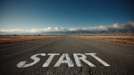Wide-angle view of an open road with a "START" marking in the foreground, set against a vast blue sky and distant horizon, evoking a sense of motivation and cinematic realism.の素材
