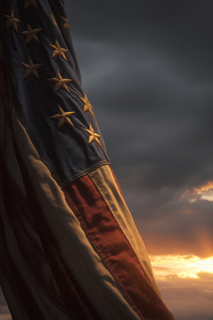 A close-up of an American flag illuminated by the last rays of sunset, set against a dramatic sky. The image conveys an emotional and reverent tone, captured in fine art realism.の素材