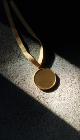 A minimalist flat lay of a gold medal on a textured black surface, highlighted by a dramatic spotlight. The high contrast and editorial style create a striking visual impact.の素材