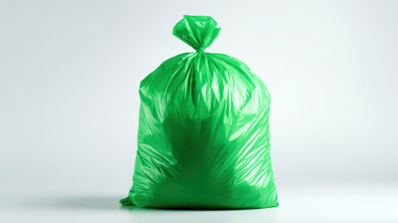 A filled green trash bag is isolated on a white background, highlighting waste collection and eco-education. The strong studio light reflection emphasizes the bag's texture.の素材