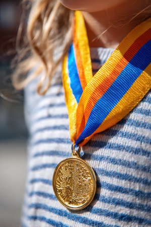 Photorealistic macro image of a gold medal hanging from a vibrant ribbon around a child's neck. Captured in bright daylight with a clean background, highlighting intricate details.の素材