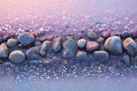 Photorealistic image of river stones rimmed with frost, reflecting a pink sunrise. Thin water flow adds to the tranquil winter texture, capturing the crisp clarity of the air.の素材
