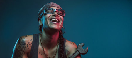 A joyful woman with tattoos and a bandana laughs heartily while holding a wrench. The studio lighting highlights her expressive features and unique style, creating a vibrant portrait.の素材