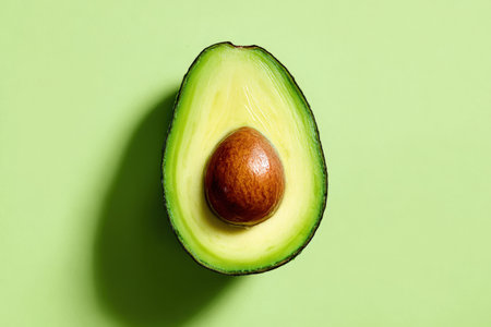 A whole ripe avocado sliced into a fan shape, isolated on a pastel green background. The high contrast highlights the avocado's vibrant green and brown hues.の素材