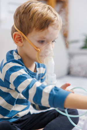 Young Child Using Nebulizer for Respiratory Treatment at Homeの写真素材