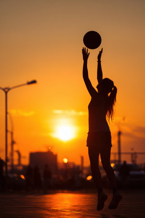 Silhouette of a teen girl shooting a basketball on an outdoor court at sunset. The warm orange sky highlights her form and motion, creating a dynamic and inspiring scene.の素材
