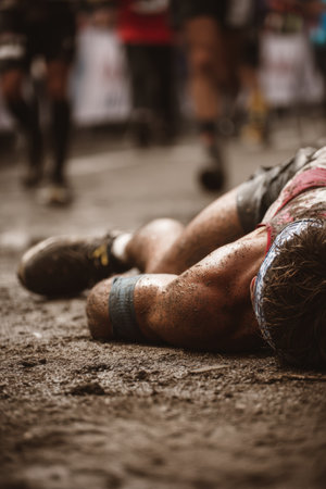 A marathon runner collapses on the ground, covered in dirt, experiencing exhaustion and emotional release after completing the race. The image captures the raw intensity of the moment.の素材