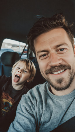 A cheerful man takes a selfie in a car, capturing a lighthearted moment as a child in the backseat playfully sticks out their tongue, creating a fun family road trip memory.の素材
