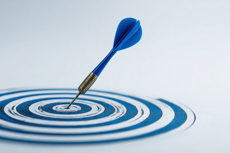 A blue dart precisely hits the bullseye on a target, set against a minimalist white background. This image symbolizes precision, success, and focus in a modern photography style.の素材