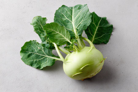 A fresh, whole kohlrabi with vibrant green leaves is placed on a neutral surface, ideal for natural food branding and organic produce promotions.の素材