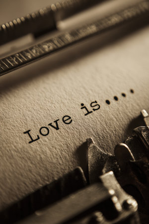 Artistic close-up of typewritten words "Love isâ¦" on a vintage typewriter. Captured in a cinematic sepia tone, the image evokes delicate emotional stillness and nostalgia.の素材
