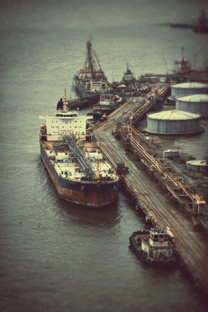 Stylized retro 1970s industrial port scene featuring a tanker at the pier. The image has a grainy texture and desaturated tones, captured from an elevated oblique angle for a nostalgic look.の素材