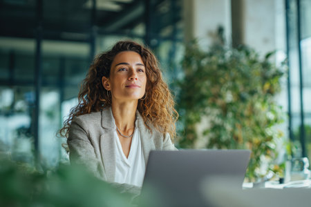 A confident entrepreneur uses a laptop in a modern co-working space. The setting is bright with natural daylight, creating a fresh and productive atmosphere.の素材