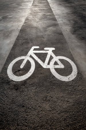A clean, minimalist image featuring a white bicycle symbol painted on a dark gray concrete lane. Ideal for catalog or design usage, highlighting simplicity and urban themes.の素材