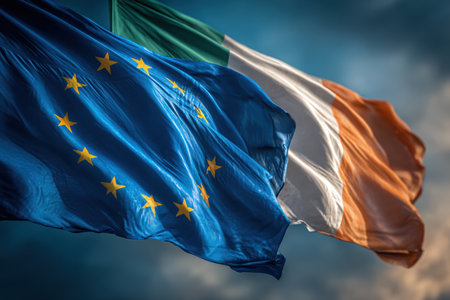 European Union and Ireland flags wave together under bright midday light, showcasing vibrant blue and green-white-orange colors. The scene conveys a warm, cooperative atmosphere.の素材