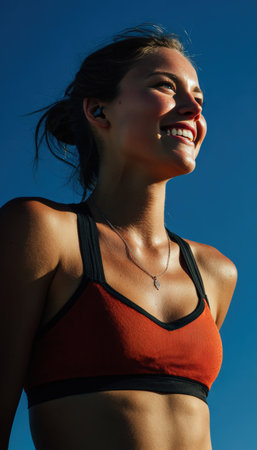 A woman athlete smiles brightly in daylight after training, set against a clear blue sky. The cinematic composition highlights her joyful expression and athletic physique.の素材