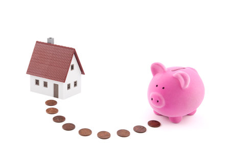 Saving for a house. Piggy bank with coins and house miniature.の写真素材
