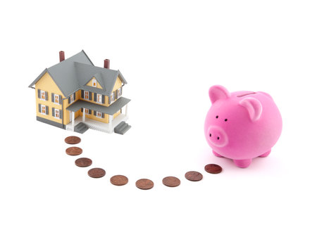Saving for a house. Piggy bank with coins and house miniature.の写真素材