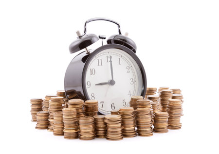 Time is money. Alarm clock with stacks of coins. Clipping path included.