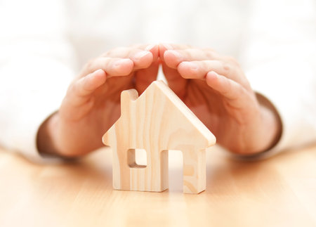 Wooden toy house protected by handsの写真素材