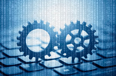 Two gears on computer keyboard with computer code in the backgroundの写真素材